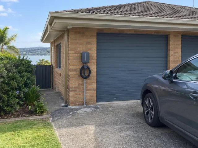 EV charger mounted on a brick garage wall beside a driveway and roller door in Umina Beach