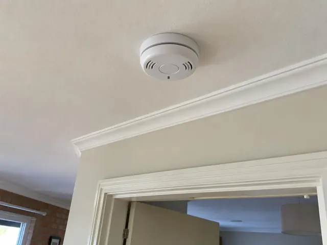 Ceiling-mounted smoke alarm above a doorway in a painted home interior in Woy Woy